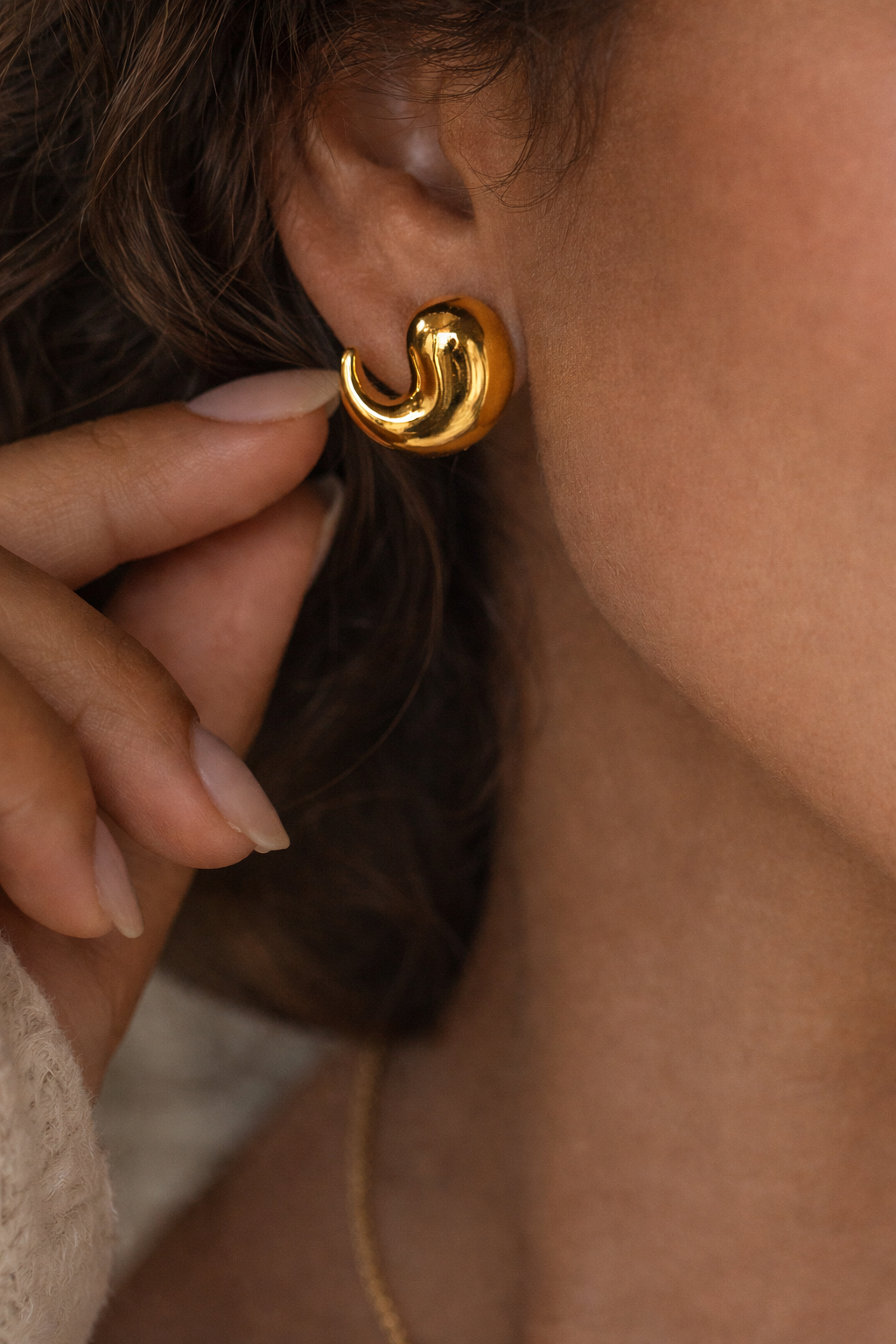 Close-up of a person wearing Bold Luxe Gold Stud Earrings, showcasing shiny, sculptural gold jewellery with a smooth, modern design on the earlobe.