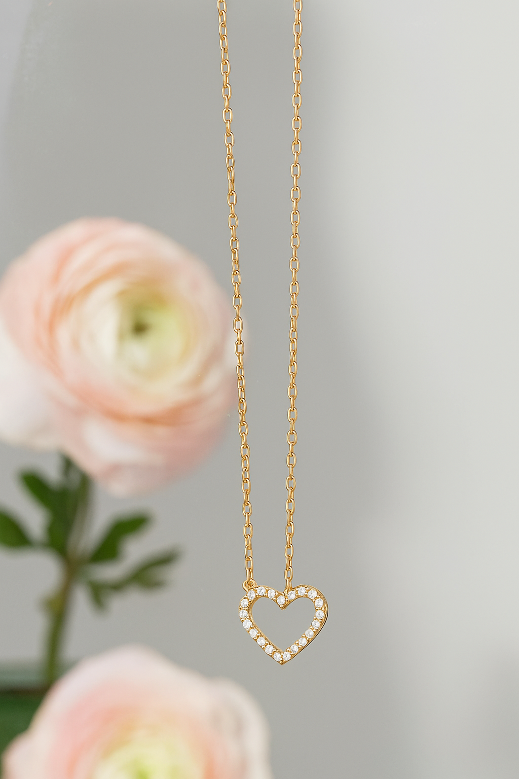 Stoned Heart Pendant Necklace featuring a delicate gold chain with a heart-shaped pendant adorned with small sparkling stones, styled against a soft floral background.