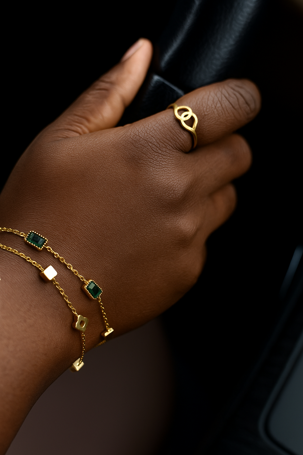 Close-up of a hand wearing gold rings and a Simple braclet stack featuring delicate gold chains with green stone and geometric charms, highlighting elegant luxury accessories.