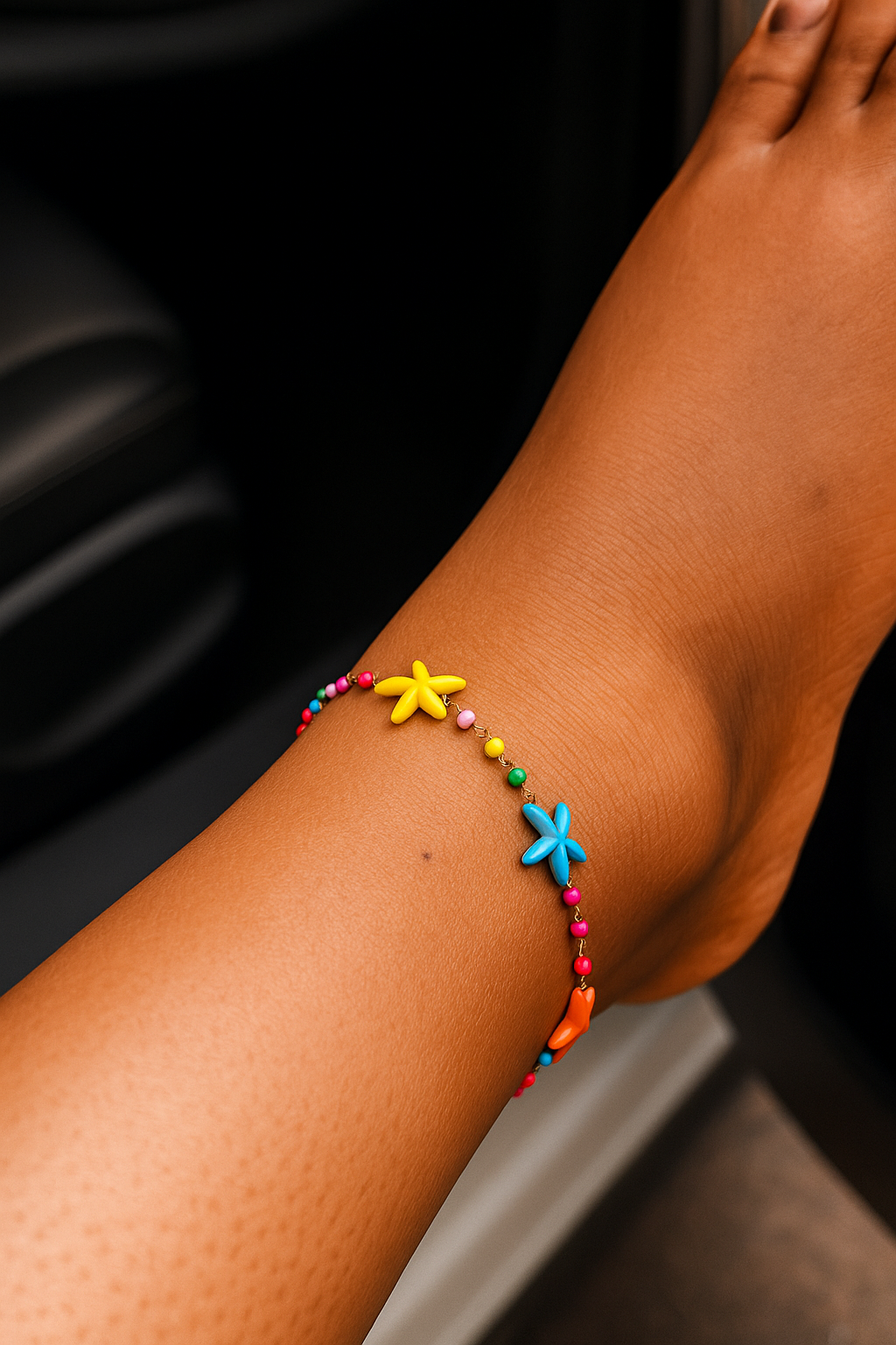 Close-up of a wrist wearing a multicolored anklet featuring small beads and flower-shaped charms in vibrant colors, showcasing a playful and stylish accessory look.