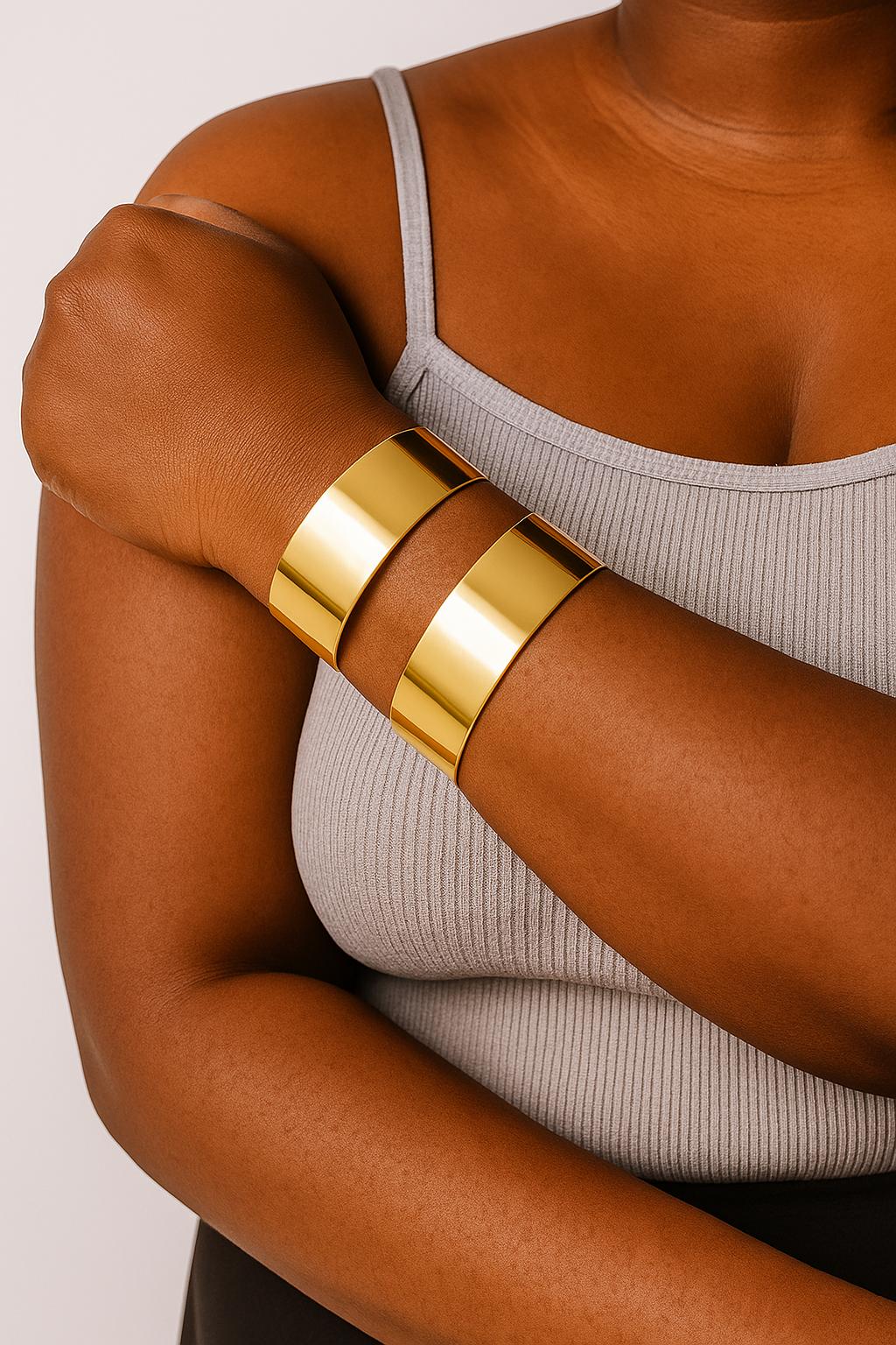 Close-up of a person wearing two shiny gold Space cuff bangles on their forearm, paired with a light gray sleeveless ribbed top.