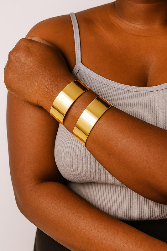 Close-up of a person wearing two shiny gold Space cuff bangles on their forearm, paired with a light gray sleeveless ribbed top.