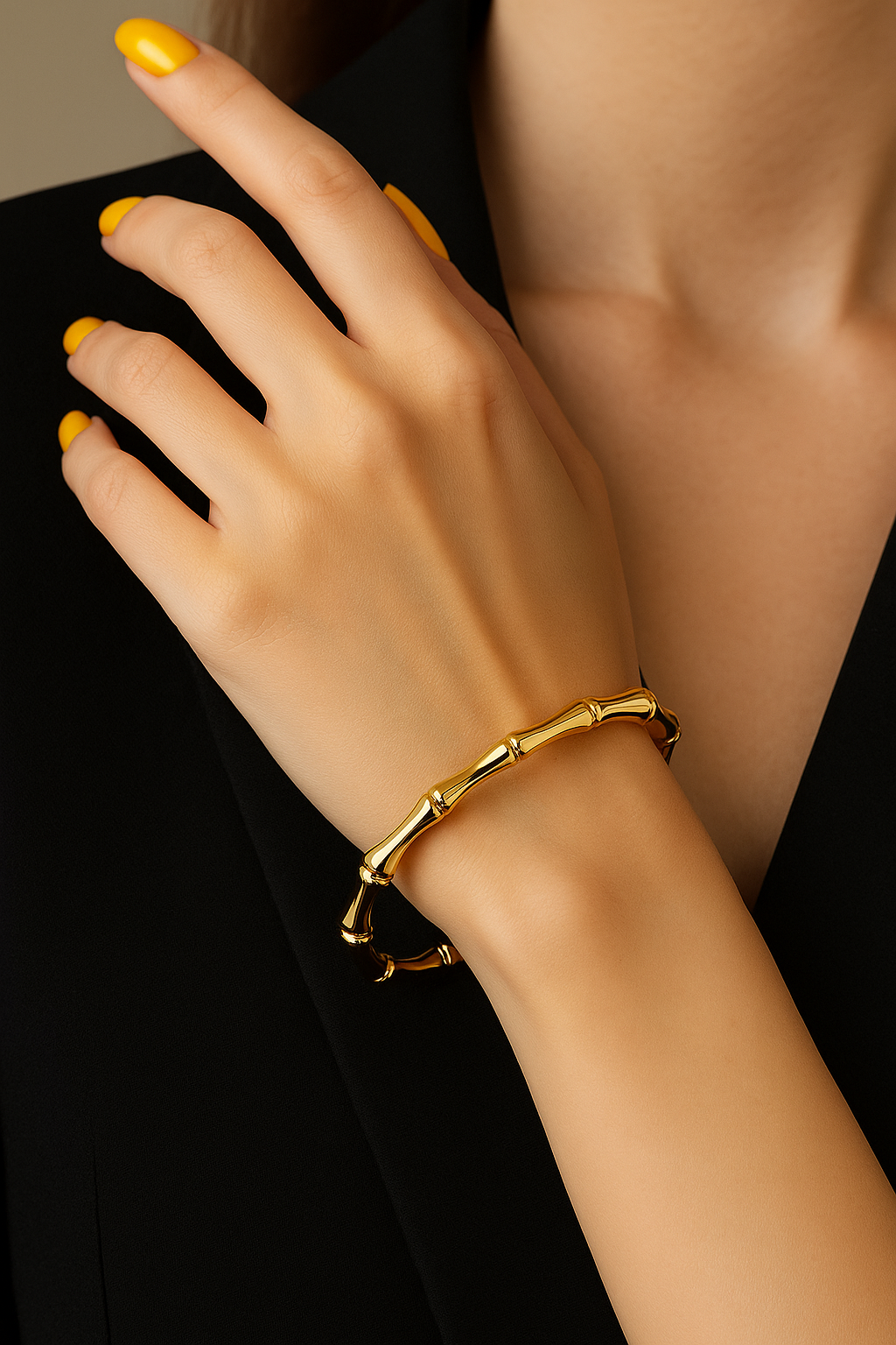Close-up of a hand with yellow nail polish wearing a shiny gold Bamboo style bangle, styled with a black outfit for a sleek, elegant look.