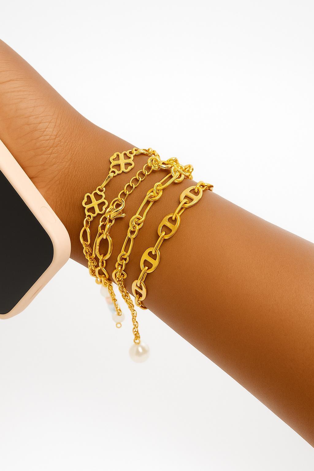 Close-up of a wrist wearing the Baddie Bracket Stack, a set of layered gold chain bracelets featuring different link styles and a small pearl charm, styled with a beige smartwatch.
